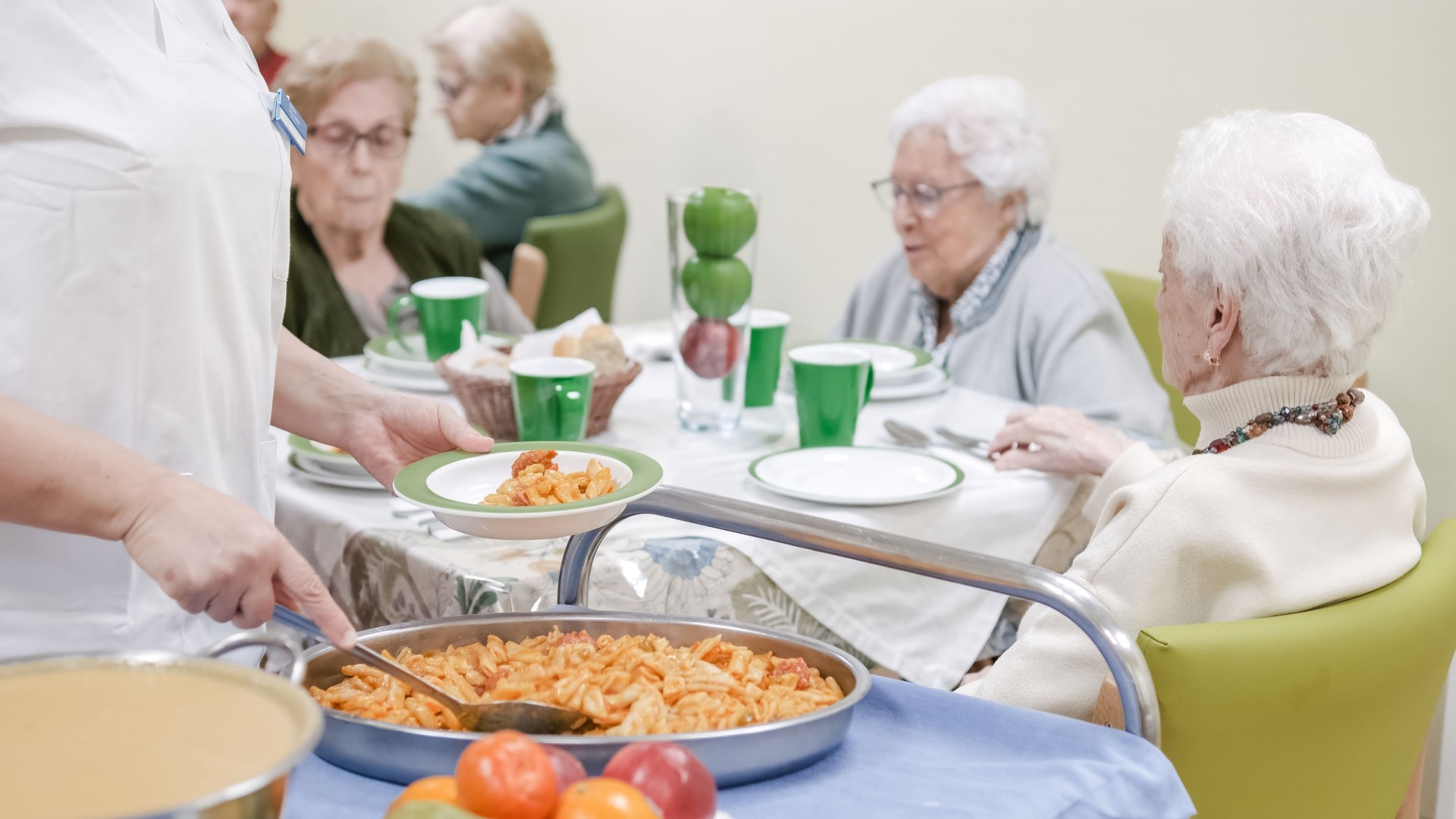 Caregiver serving pasta to senior people at nursing home